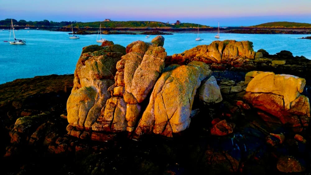 Granitfelsen in der Abenddämmerung, im Hintergrund ankernde Segelboote