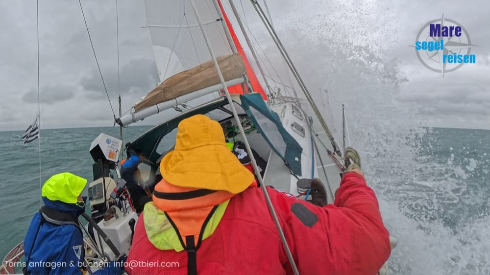 Crew in Ölzeug am Steuer, Gischt spritzt bei rauer See über das Deck