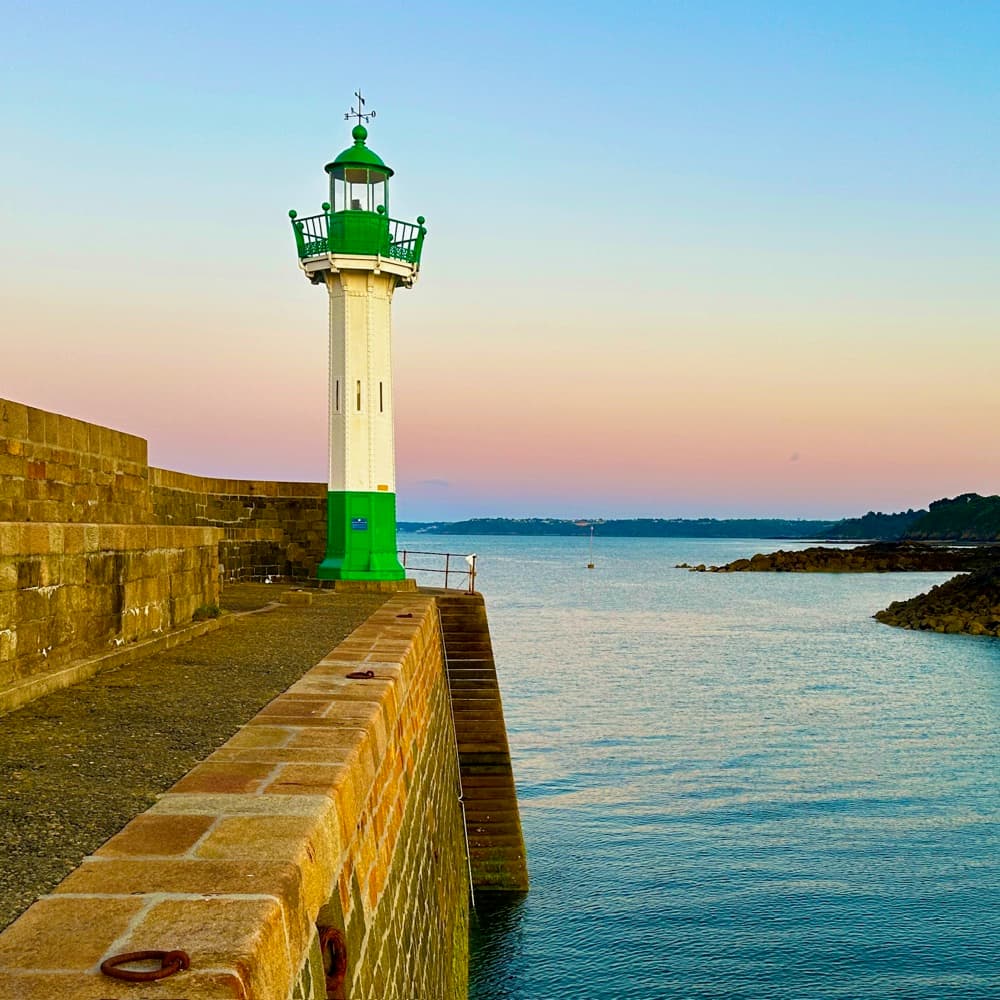Grün-weisser Leuchtturm am Ende einer Hafenmole aus Stein in der Abenddämmerung