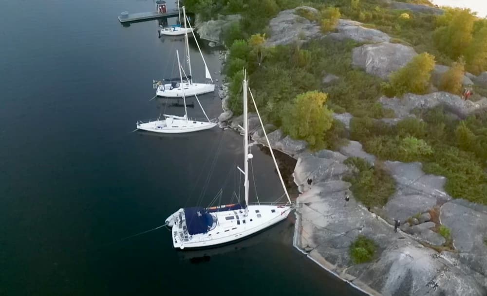 Segelyachten liegen mit Landleinen direkt an den Granitfelsen einer bewaldeten Insel